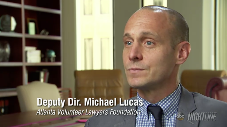 A man in a suit sits in an office with shelves in the background. The text on the image reads, "Deputy Dir. Michael Lucas, Atlanta Volunteer Lawyers Foundation.