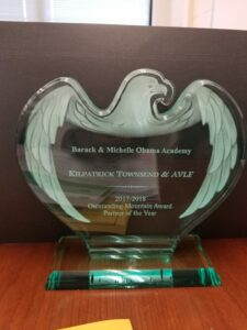 A glass award shaped like an eagle with the text: "Barack & Michelle Obama Academy, Kilpatrick Townsend & AVLF, 2017-2018 Outstanding Mountain Award, Partner of the Year." The award rests on a wooden surface.