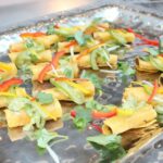 A tray of garnished taquitos topped with avocado slices, bell pepper strips, cilantro, and onions.