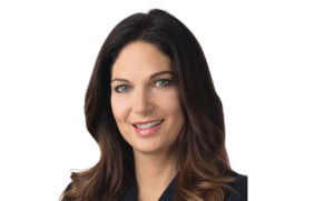 Portrait of a smiling woman with long, dark hair, wearing a black top against a white background.