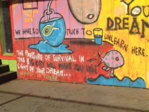 A colorful graffiti mural with text and illustrations. A fishbowl with an eyeball, a smaller fish with an eye, and text: 