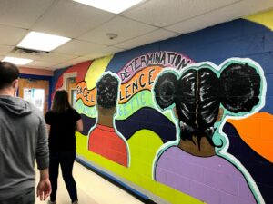 A vibrant mural in a hallway features two people with colorful outlines. Words like 