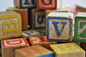 Close-up of colorful wooden toy blocks with letters, showing signs of wear. The letters V, H, B, and Z are visible on front-facing blocks, while other blocks display sides with letters like D and H. The blocks are stacked, creating a playful and nostalgic scene.