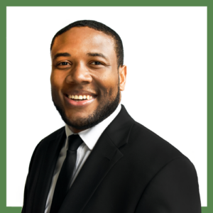 A man in a black suit and tie smiles warmly against a white background. The image is in a square frame.