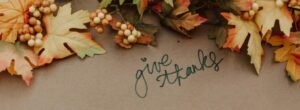 A fall-themed arrangement with colorful autumn leaves and clusters of small berries surrounds the handwritten phrase 