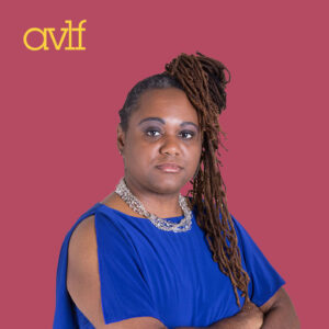 Person with long, styled hair wearing a blue dress and silver necklace. Stands confidently against a pink background with the AVLF logo in the corner.