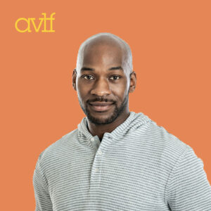A man in a striped shirt stands against an orange background with the letters 