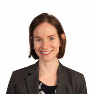 A woman with short brown hair, wearing a dark blazer over a floral top, smiles at the camera against a plain white background.