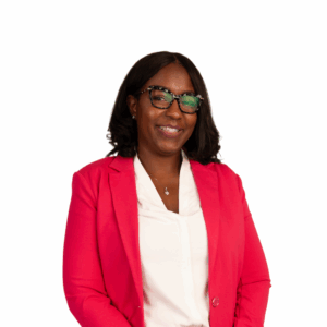 A woman with shoulder-length dark hair, wearing glasses, a white blouse, and a bright pink blazer, smiles confidently against a plain white background.