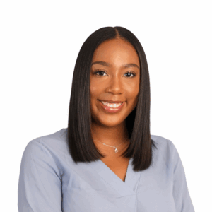 A woman with straight, shoulder-length black hair smiles at the camera. She is wearing a light blue blouse, a small pendant necklace, and has a nose ring. The background is plain white.