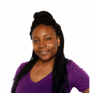 A smiling woman with long braided hair wears a purple V-neck shirt and a necklace, posing confidently against a plain white background.