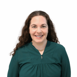 A woman with long, curly brown hair smiles at the camera. She is wearing a dark green top and a gold necklace, standing against a plain white background.