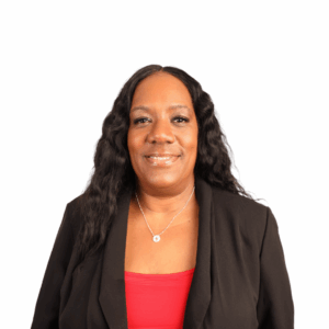 A woman with long wavy black hair, wearing a black blazer over a red top and a silver necklace, smiling at the camera against a plain white background.