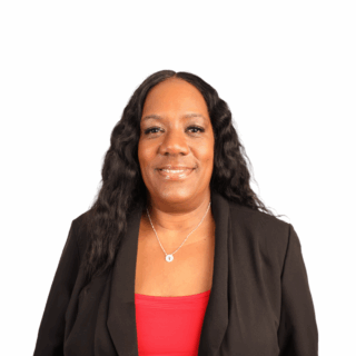 A woman with long wavy black hair, wearing a black blazer over a red top and a silver necklace, smiling at the camera against a plain white background.