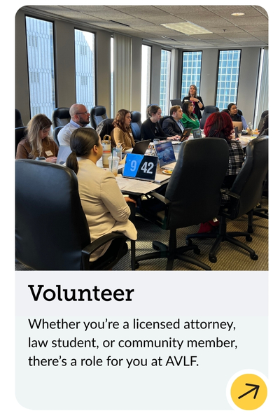 A diverse group of people sitting in a conference room around a table with laptops, appearing engaged in a discussion or training session. A sign with the number 42 is visible. Large windows show a cityscape. Text below encourages volunteering at AVLF.