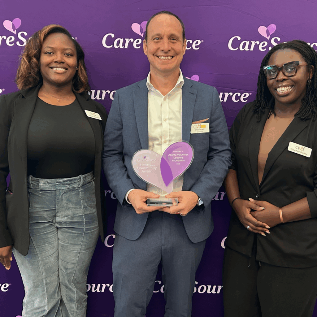 Three people smile and pose for a photo in front of a purple CareSource backdrop. The person in the center holds a heart-shaped award, while the two others stand on either side, all wearing name badges.