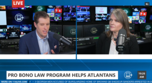 Two news anchors sit at microphones in a studio, discussing a pro bono law program helping Atlantans. News headlines and graphics are displayed on screens behind them, with a ticker running at the bottom.