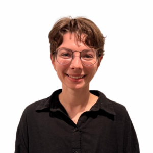 A person with short brown hair, wearing round glasses and a black collared shirt, is smiling against a plain white background.