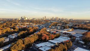 Aerial view of Atlanta, Georgia at sunset, showing the city skyline in the distance, highways, and residential areas surrounded by autumn trees in the foreground.